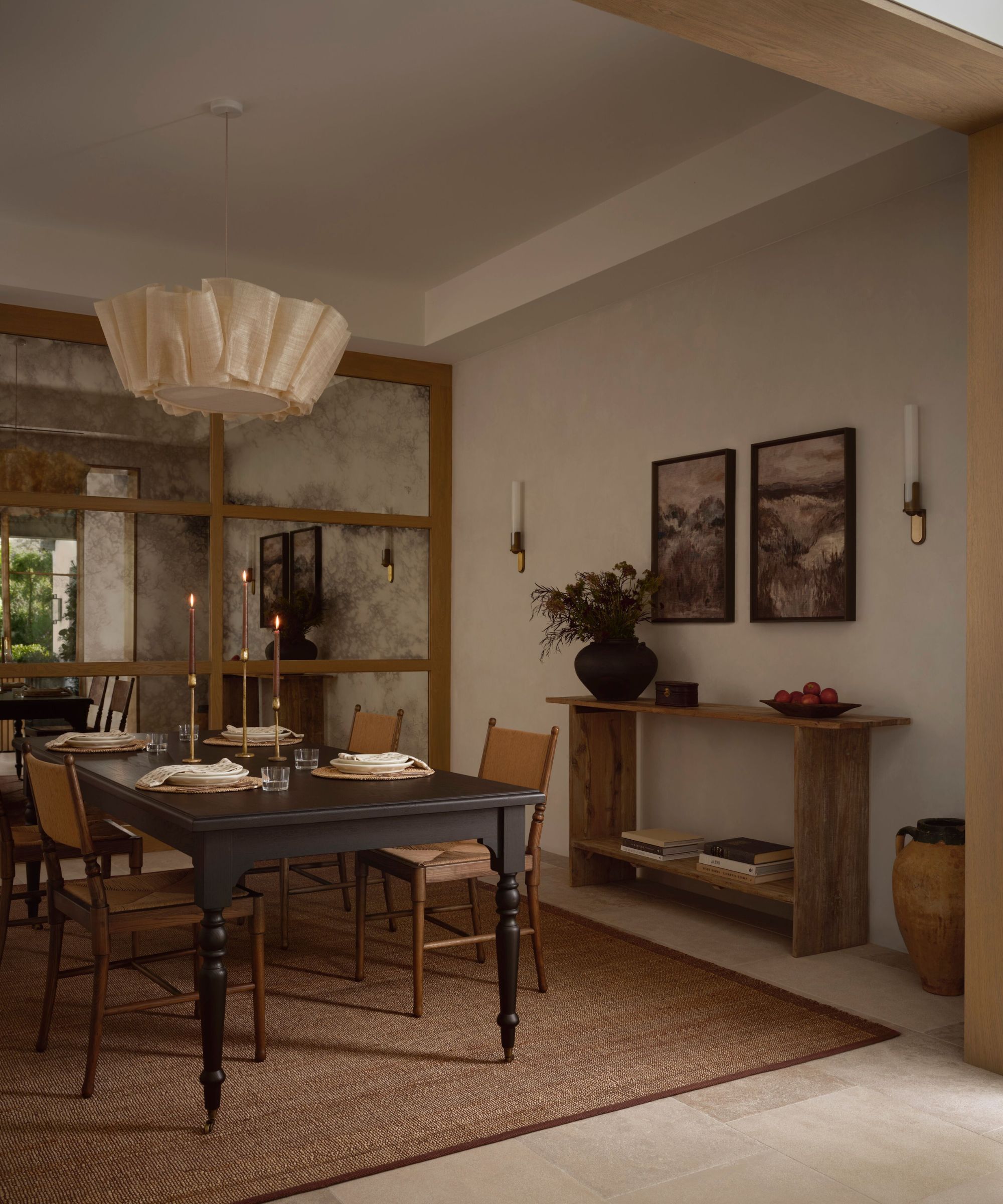 Warm neutral dining room with jute rug, mirrored panelling, a black wooden dining table, rattan brown dining chairs, a wooden console table pushed against the wall, and a pleated pendant light.