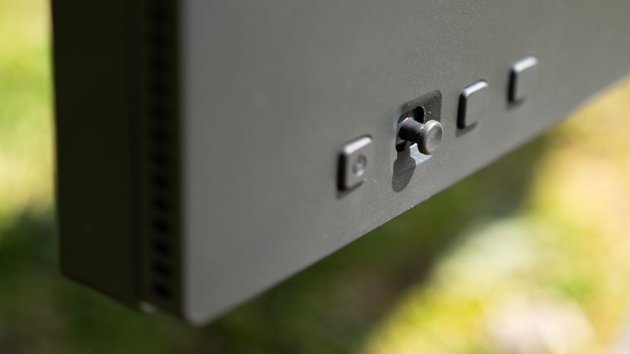 A black BenQ PD3225U monitor sitting on grass in sunshine