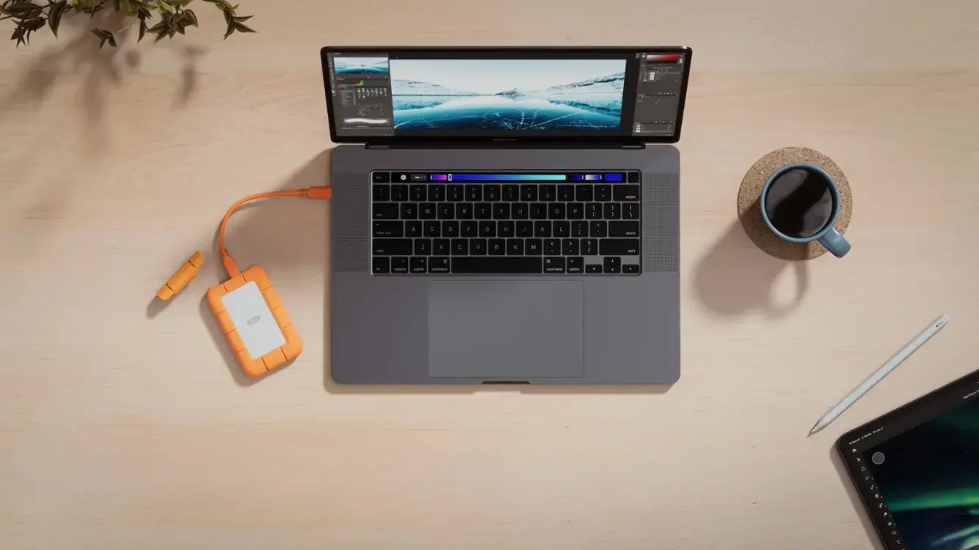 A LaCie external drive plugged into a MacBook Pro next to a cup of coffee and a pencil