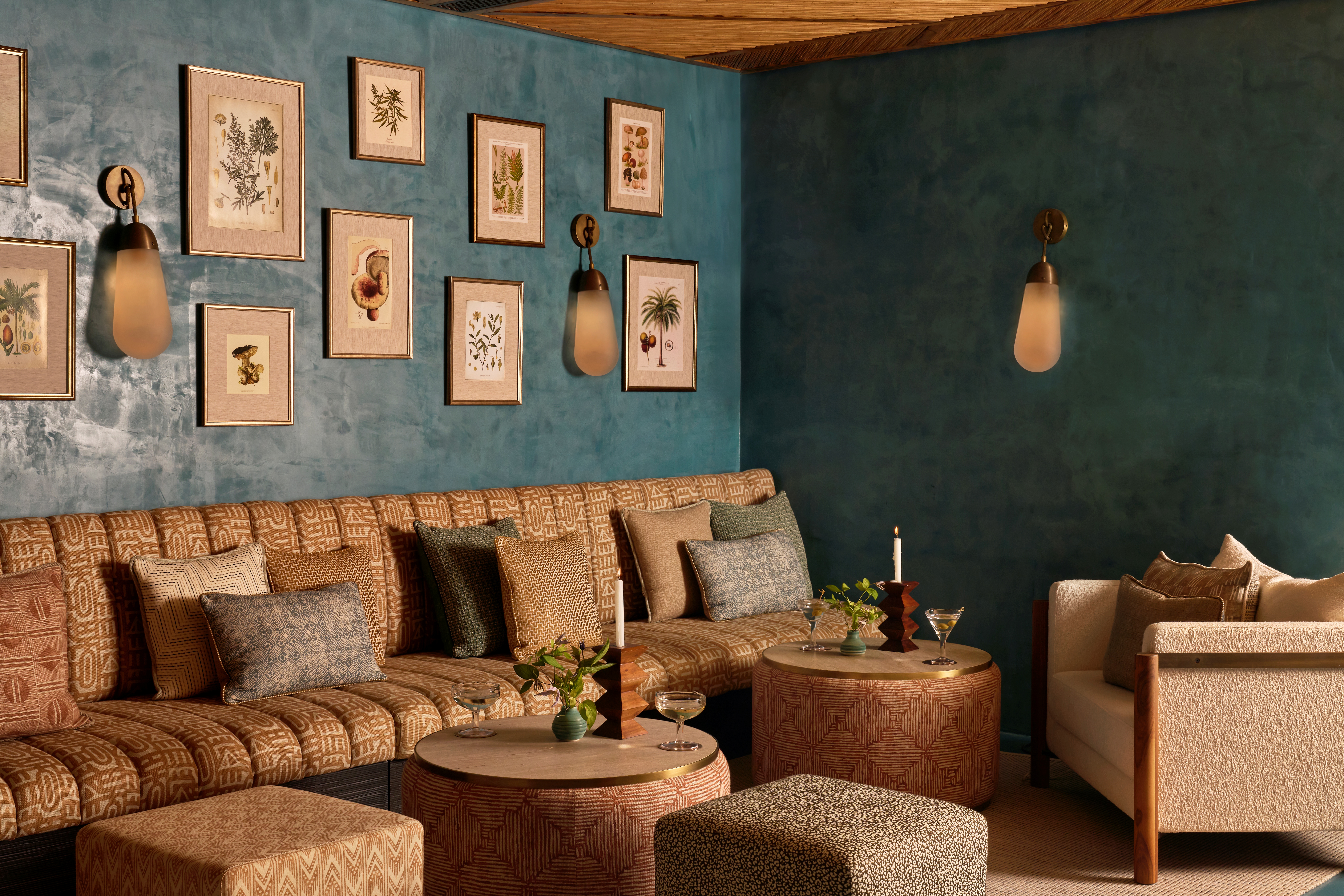 A series of interior shots of a turquoise plaster-tinted restaurant with textural walls and earthy furnishings throughout, from leathery banquettes and cream tablecloths to wooden accents, pendant lighting, and a rattan and wood ceiling.