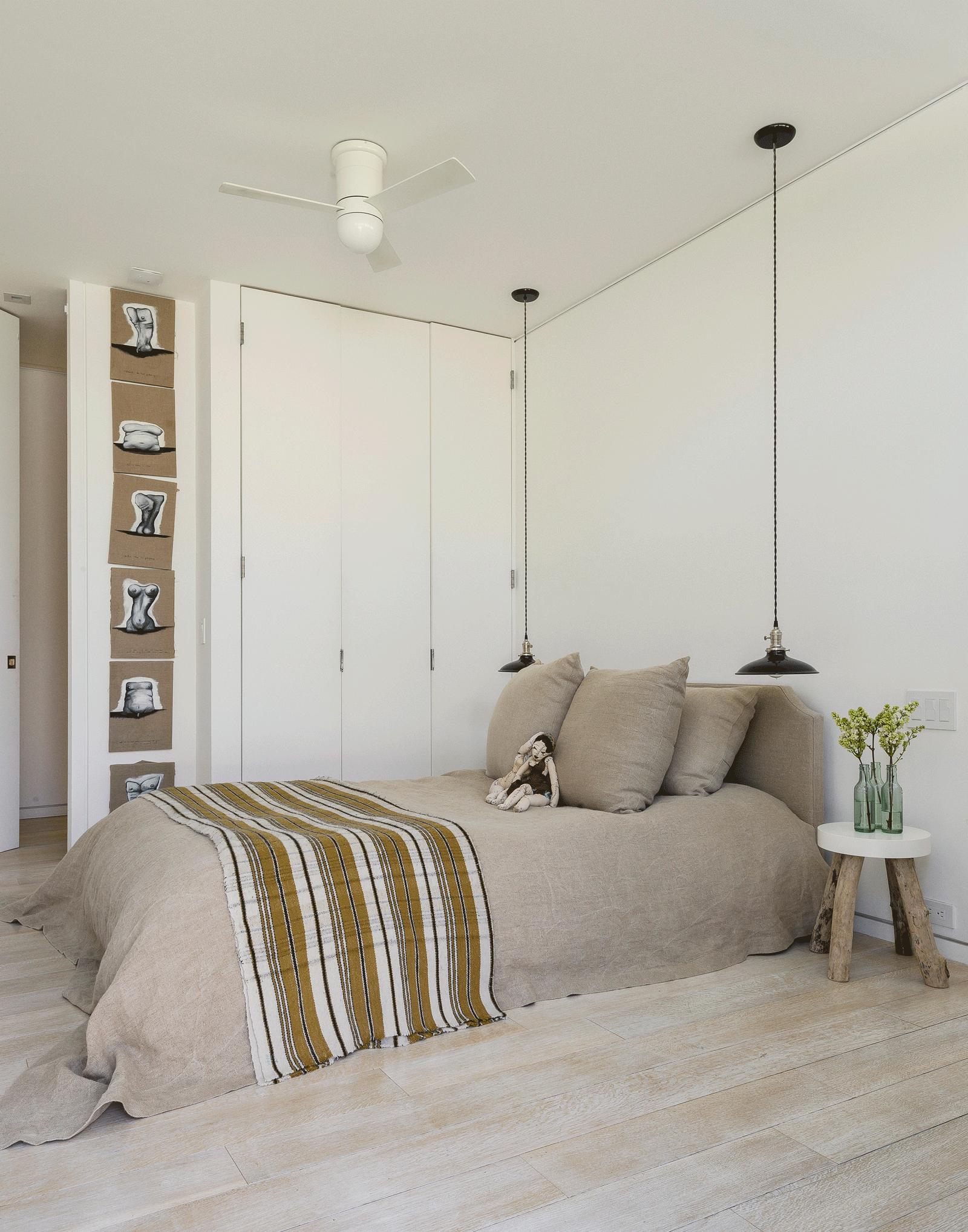 Guest bedroom with white walls and beige bedding and black pendant lights as bedside lights