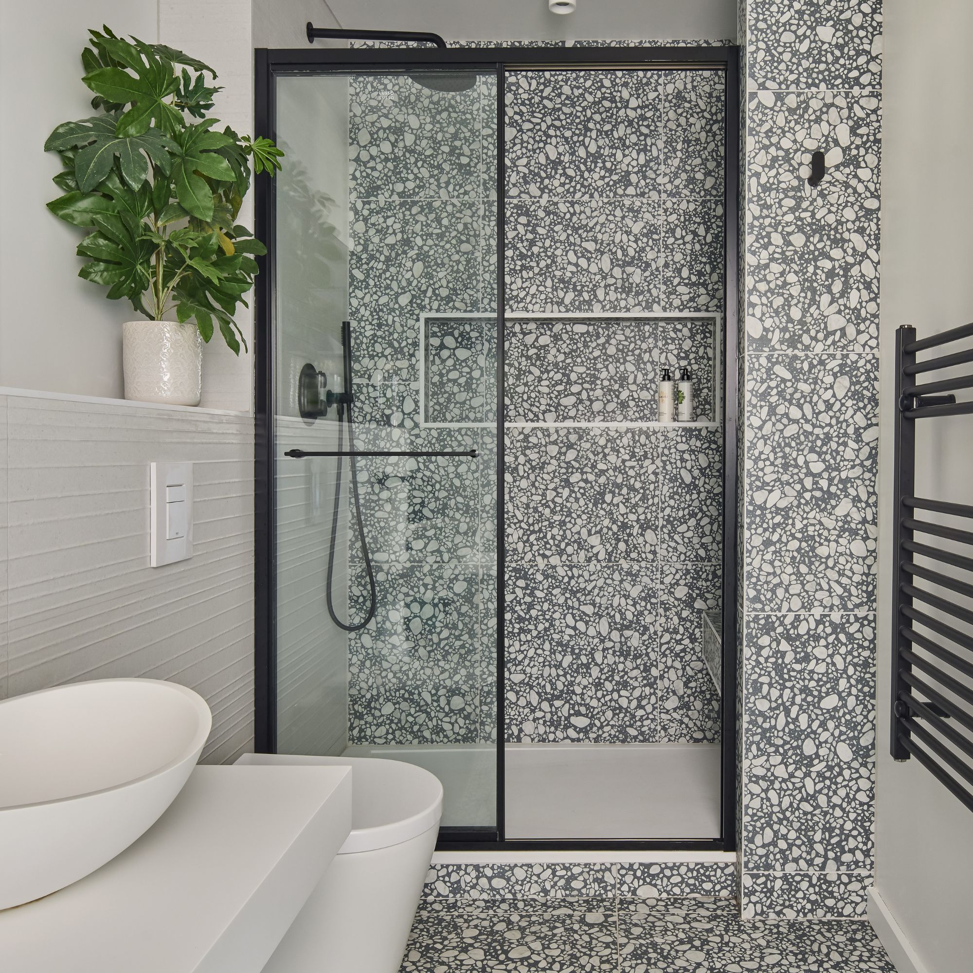 White, grey and black shower room, with grey and white patterned tiles, white sanitaryware, black shower door, black shower and black towel rail