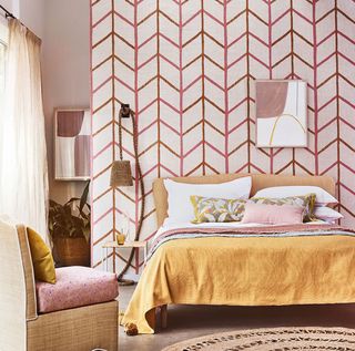 A bedroom with red and white chevron wallpaper, a yellow bed and a chair
