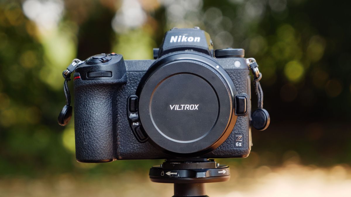 Viltrox AF 26mm F2.8 EVO 'pancake' lens attached to a Nikon mirrorless camera, there's dappled light through a tree behind it. Lens cap is on