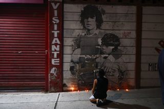 A boy kneels in front of a mural of Diego Maradona outside the stadium of Argentinos Juniors