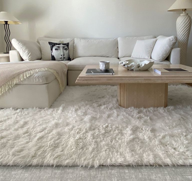 Cream shaggy rug over cream carpet in cream lounge with wooden coffee table, L-couch and cushions 