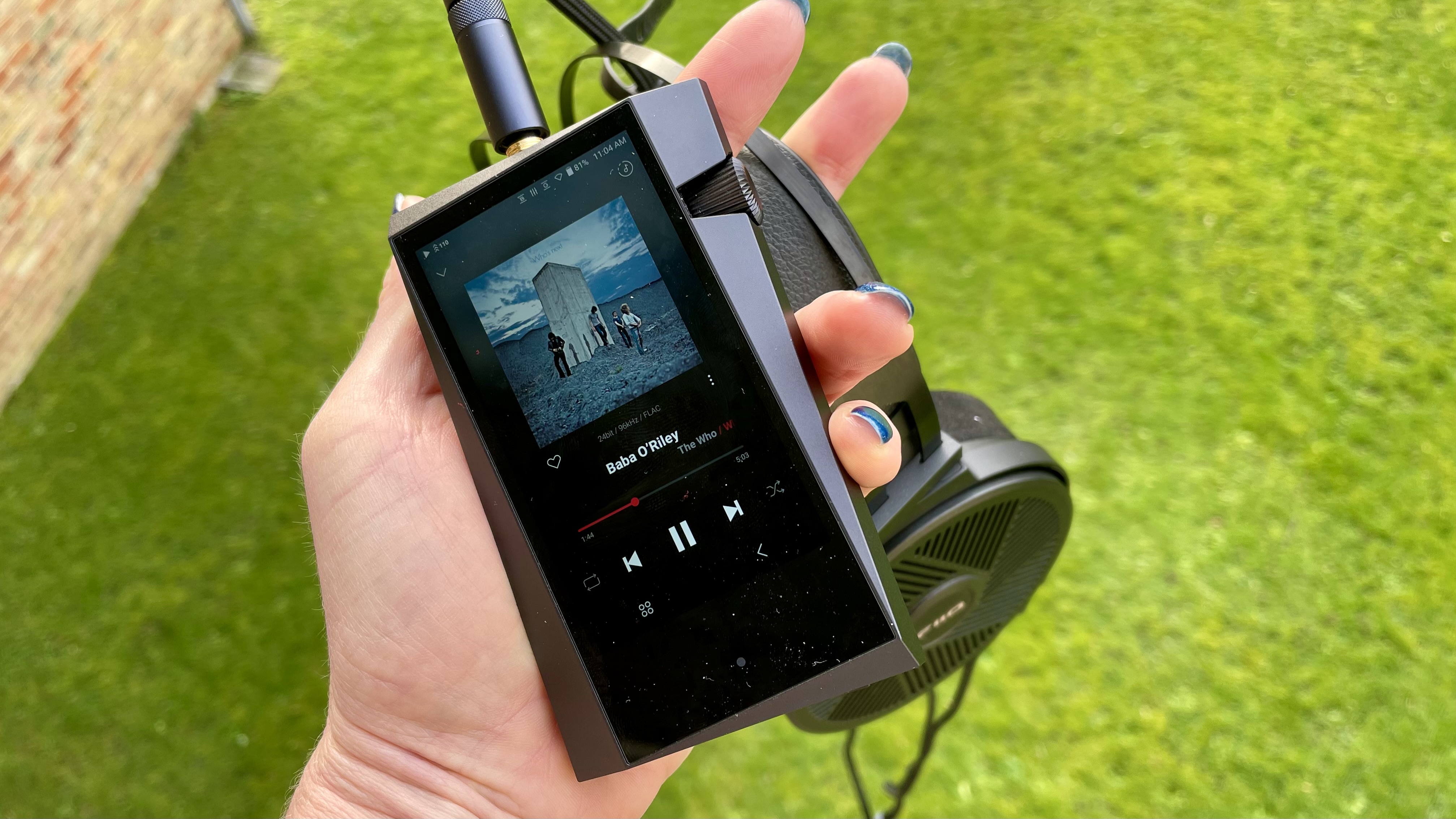 Astell & Kern A&norma SR35 held in a hand with headphones, on green background