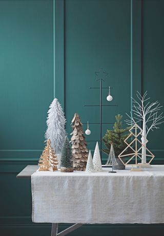 Small Christmas tree shapes, a metal structure with arms, geometric shape, star shape, triangular pine tree shapes and one real mini tree against a blue painted wall.