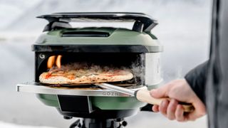 A man takes a pizza out of the Gozney Tread pizza oven