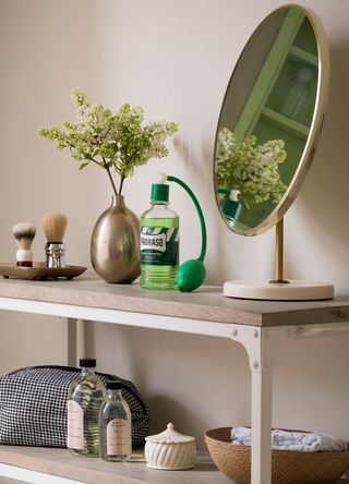 Pink bathroom with wrought iron storage unit containing a round beauty mirror and products