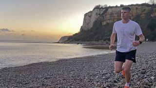 Man wearing adidas Terrex Multi Trail Running Shorts and white T-shirt on pebbly beach at sunset