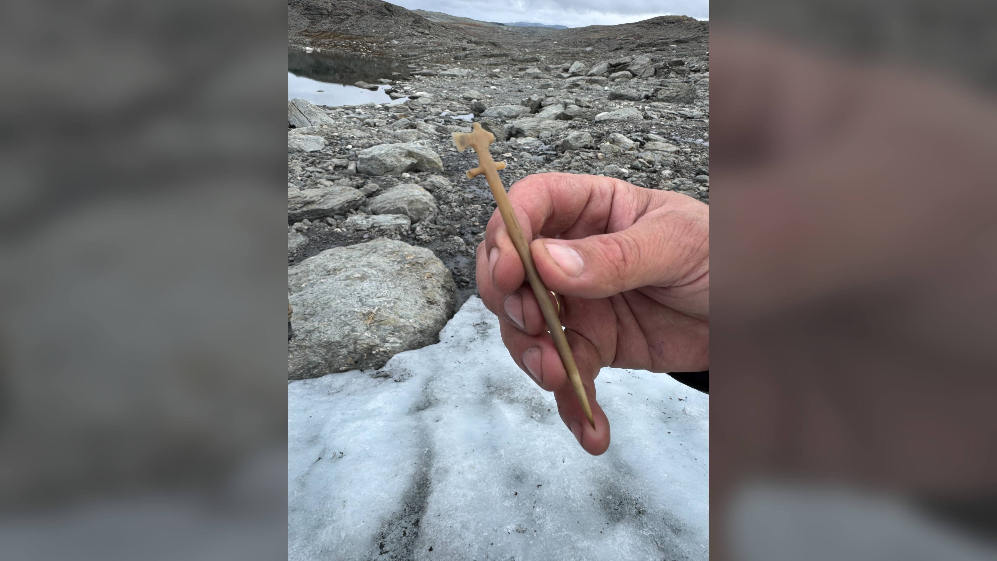 a light-skinned person holds an ax-shaped antler pin against an icy backdrop