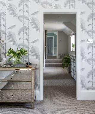 Bedroom with carpet, botanical leaf pattern light grey and white wallpaper and mirrored chest of drawers. View along an upstairs corridor.