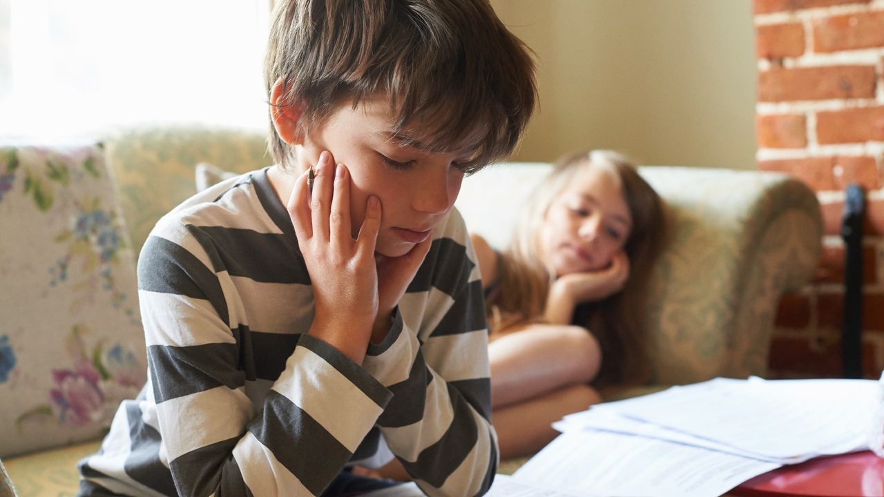 Two kids sitting on the couch at home studying school papers 