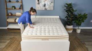 Julia Sagar with both hands on a Saatva Classic mattress on a bed frame in a bedroom scene