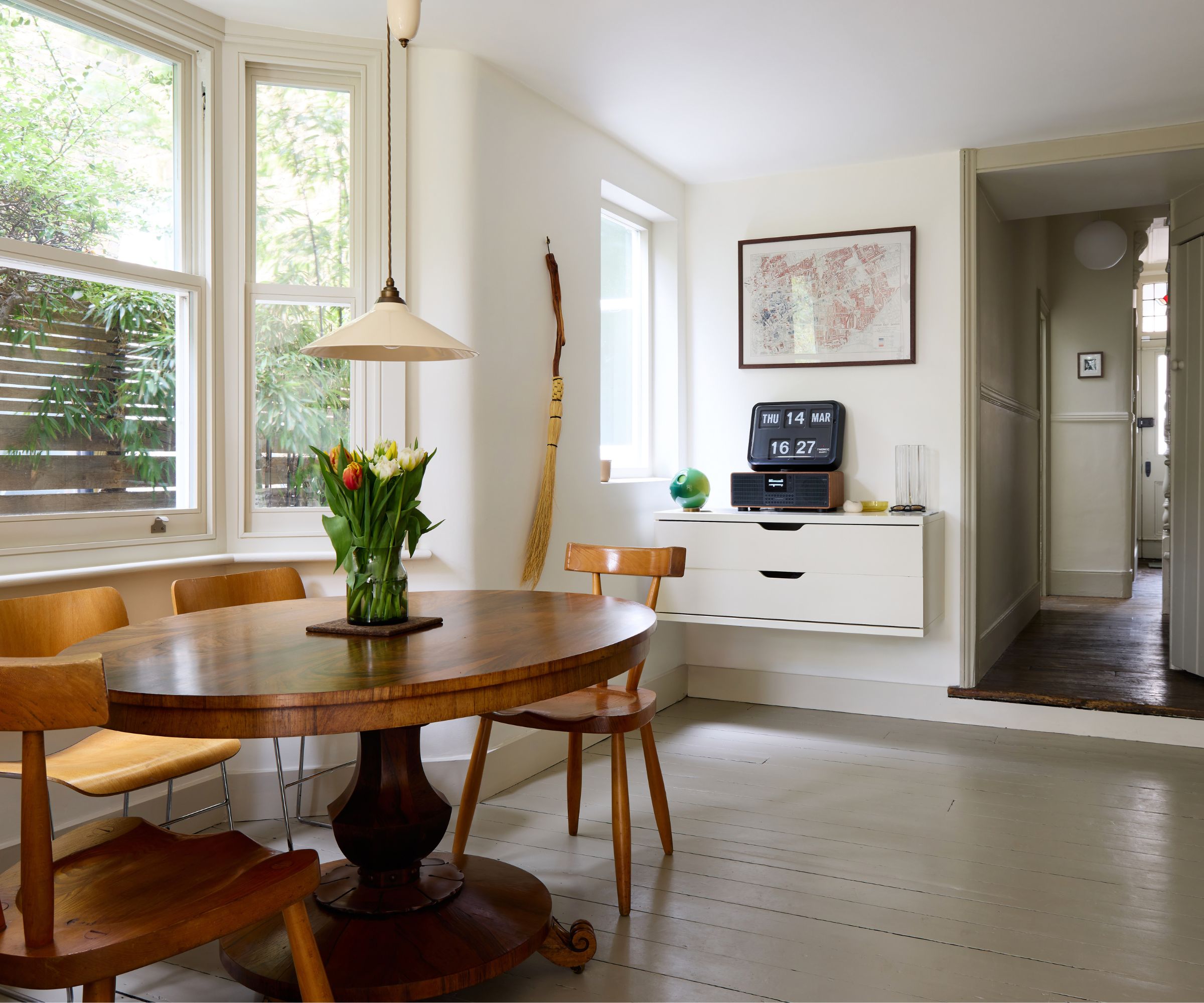 Dining room with Drop Cloth by Farrow &amp;amp; Ball painted walls, grey painted wooden floor, a midcentury dining chair, and a round wooden table with tulips in the middle
