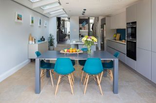 open plan modern kitchen diner with rooflights, blue dining chairs and glossy handleless cabinets
