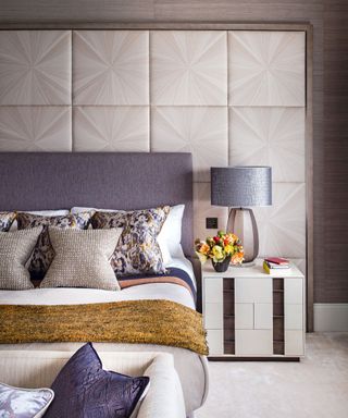 Bedroom accent wall ideas with square, modern wall panelling behind a bed with large blue headboard and mustard yellow throw.