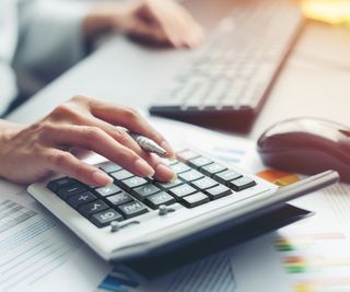 close up of female hand pressing calculator with keyboard and mouse in background on desk