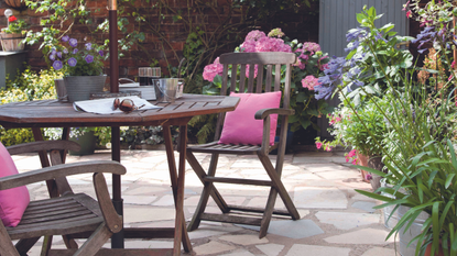 Wooden table and chairs on patio surrounded by plants and flowers