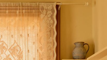 A lace curtain hanging from a white curtain rod
