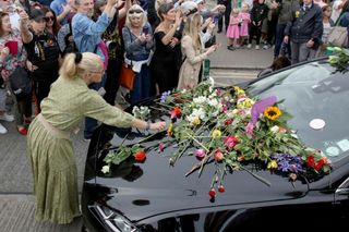 People lay flowers and tributes on the hearse during the funeral procession of late Irish singer Sinead O'Connor, outside the former home in Bray, eastern Ireland, ahead of her funeral on August 8, 2023. A funeral service for Sinead O'Connor, the outspoken singer who rose to international fame in the 1990s, is to be held on Tuesday in the Irish seaside town of Bray.