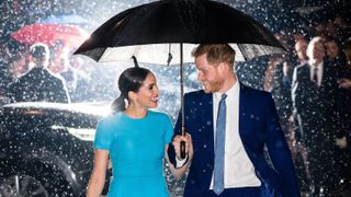Meghan Markle and Prince Harry walk through the rain sharing an umbrella.