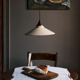 A minimalist dining setup featuring a vintage-style pendant light with a cream enamel shade and a twisted cord, suspended over a round wooden table. 