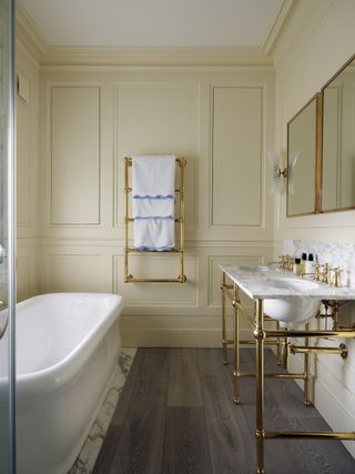 Beige panelled bathroom with a roll top bath and brass fixtures