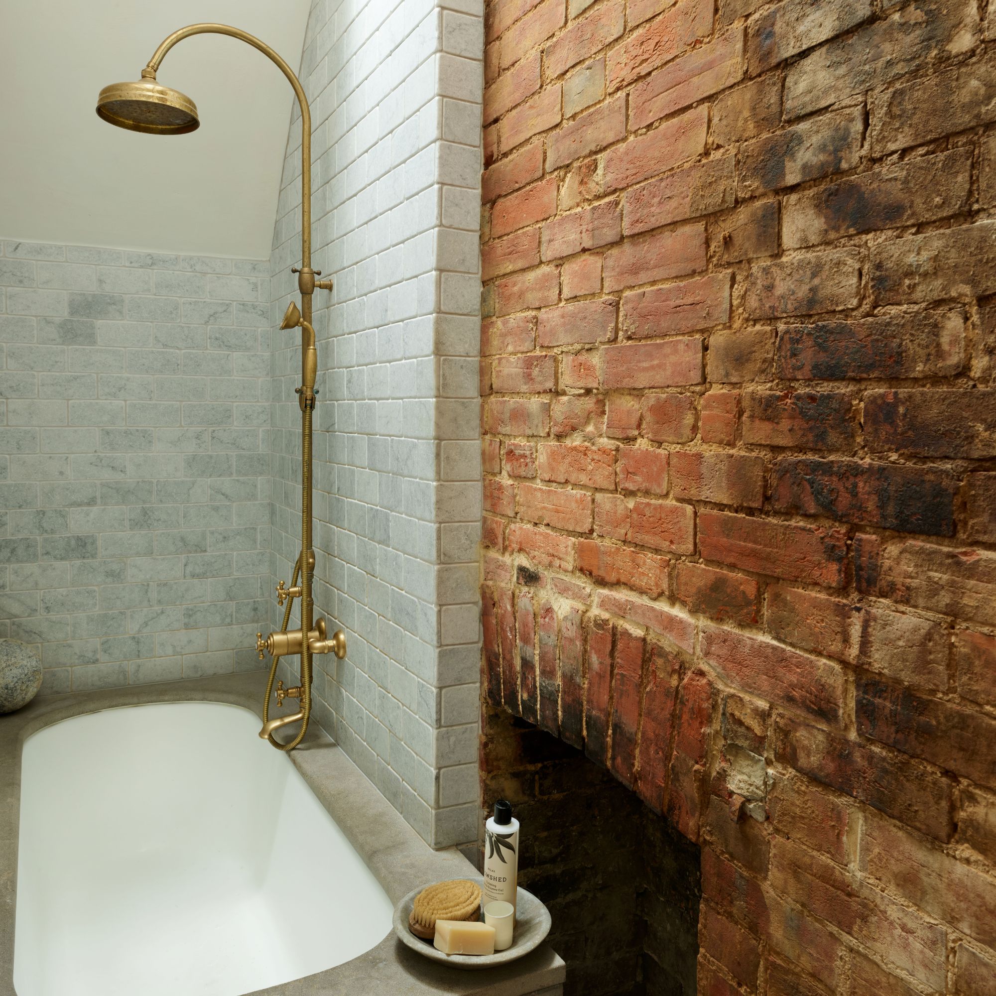 bathroom with exposed brick wall and tiled shower area over the bath