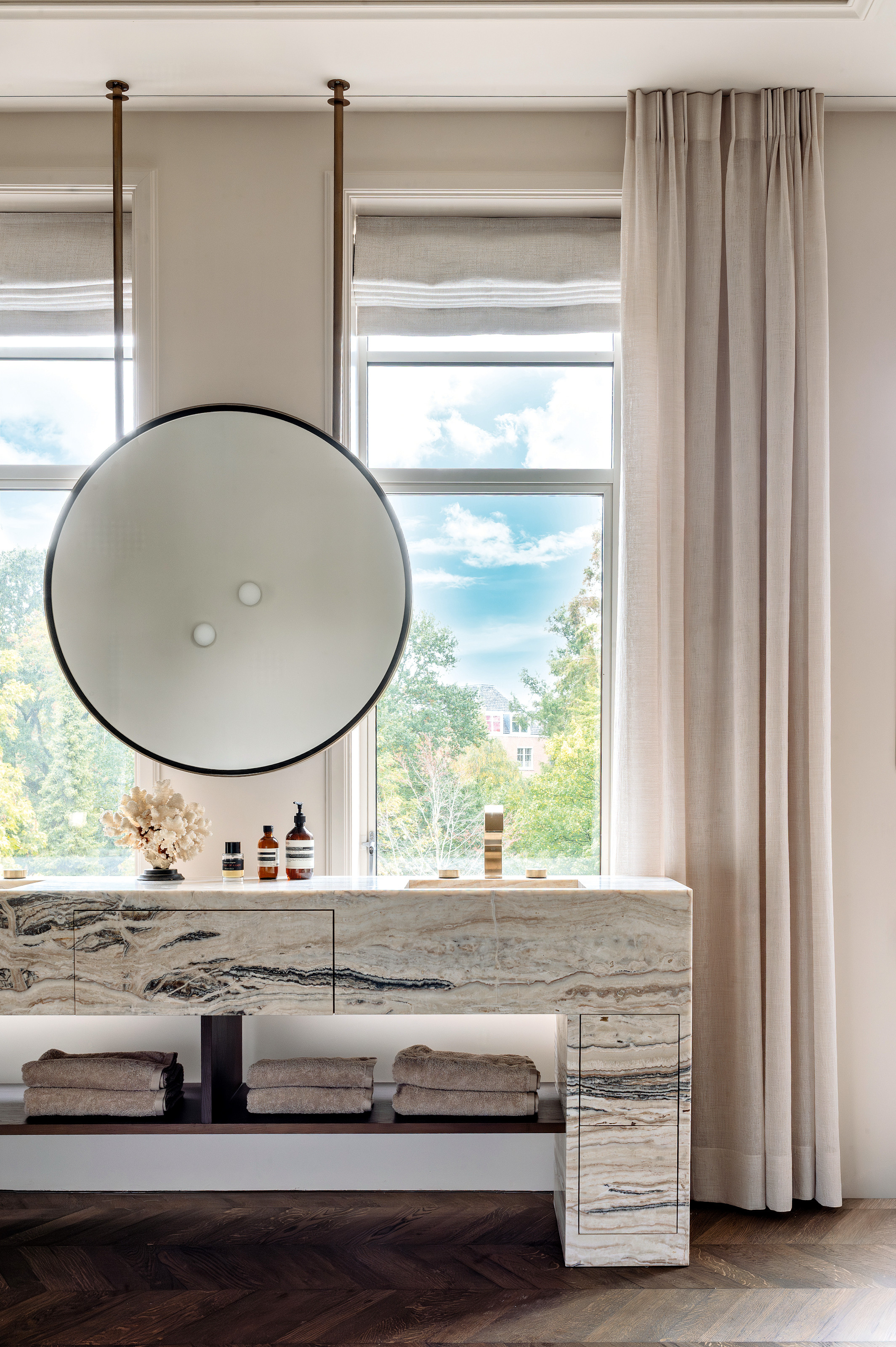 Bathroom with white and grey marble vanity, suspended round mirror and cream curtains