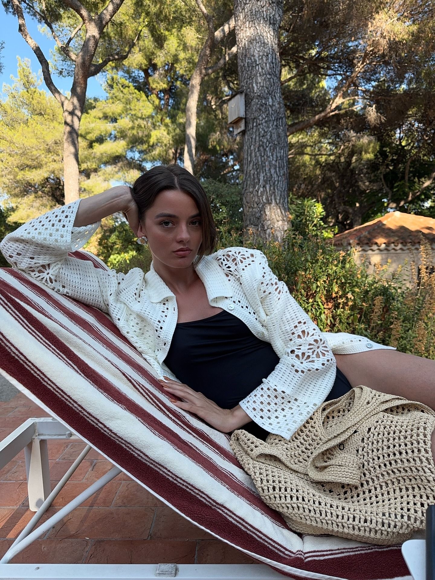 Influencer @maryljean wears a crochet cardigan over a black swimsuit with a crochet handbag.
