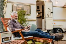 man resting on the wooden deck chair using laptop with RV behind