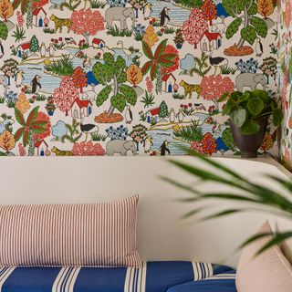 A room with a colourful animal print wallpaper on the top half and striped blue, white, and red cushions