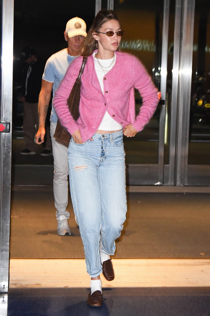 Gigi Hadid wearing a pink cardigan, white T-shirt, jeans, and loafers with socks at JFK