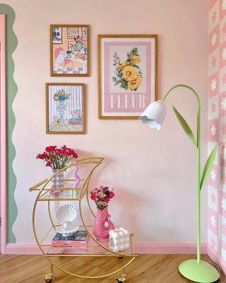 A pink wall with pictures, a moon-shaped bar cart, and a lily shaped lamp