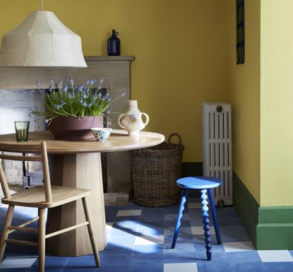A pale yellow dining space with green skirting trim and blue and white tiled floor