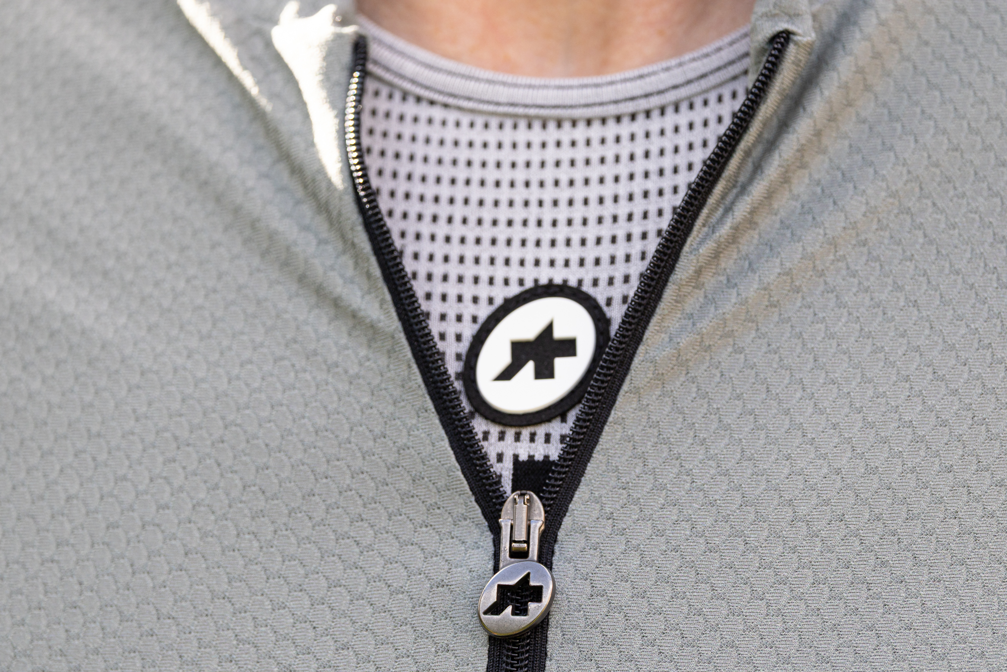 close up of the zip pull on the Assos Mille GT jersey, showing the pale green jersey and grey baselayer