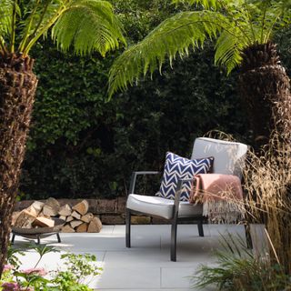 White paved path with outdoor armchair and firepit below a fern palm tree