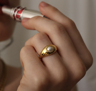 a woman applying ysl lipstick while wearing a pearl signet ring