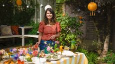 Noor Murad standing in her yard by a table set for summer with colorful tableware and accessories and yellow hanging lanterns