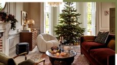 Christmas tree in the bay window of a stylish living room scene from Soho Home. There is a deep red couch, a modern white, fluffy accent chair and beige walls