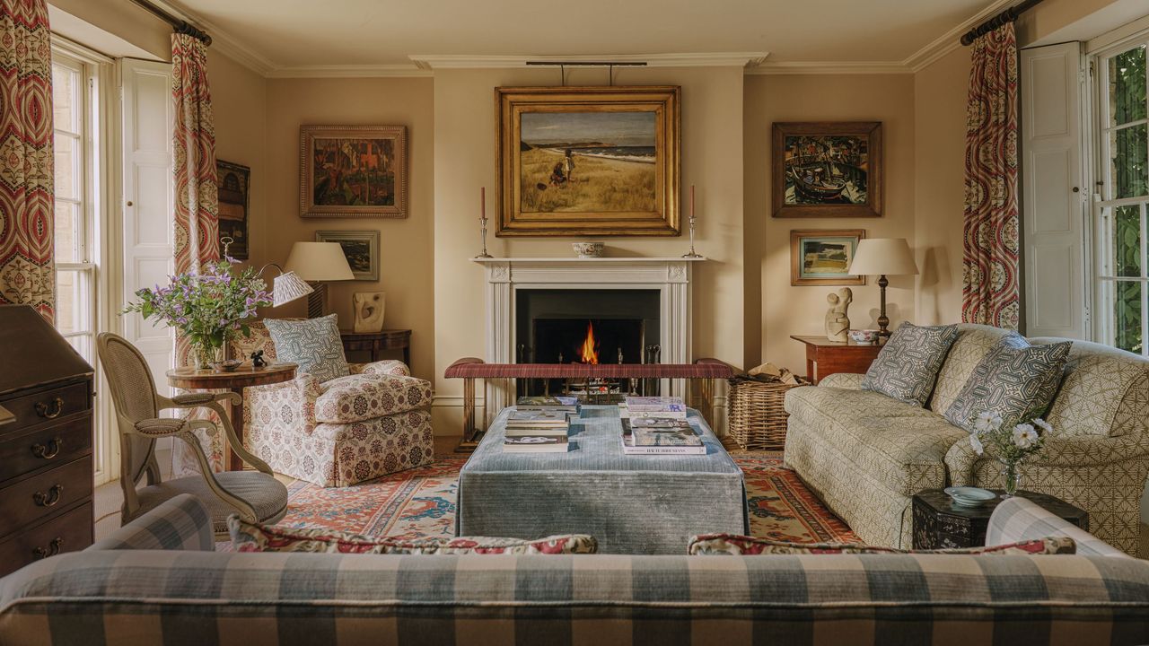 a layered cozy drawing room in the cotswolds with a lit fire, patterned sofas and vintage decor