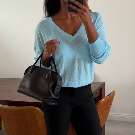 a woman wearing a blue vneck top, black pants, and black leather bag