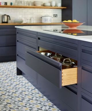 kitchen island with open drawer showing pans; hob over drawer with bowl of lemons next to it; kitchen in background; tiled floor