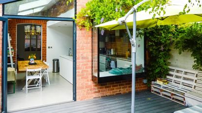 glass side return extensions on the side of a terraced brick house, and a grey deck out front