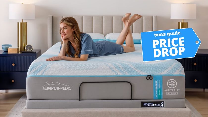 A woman in blue pyjamas laying on her stomach on the grey, white and blue Tempur-Pedic Tempur-ActiveBreeze smart bed in bedroom with two navy bedside tables and gold lamps