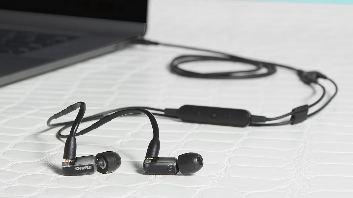 Shure Aonic 3 wired in-ear headphones in black, connected to a laptop on a table