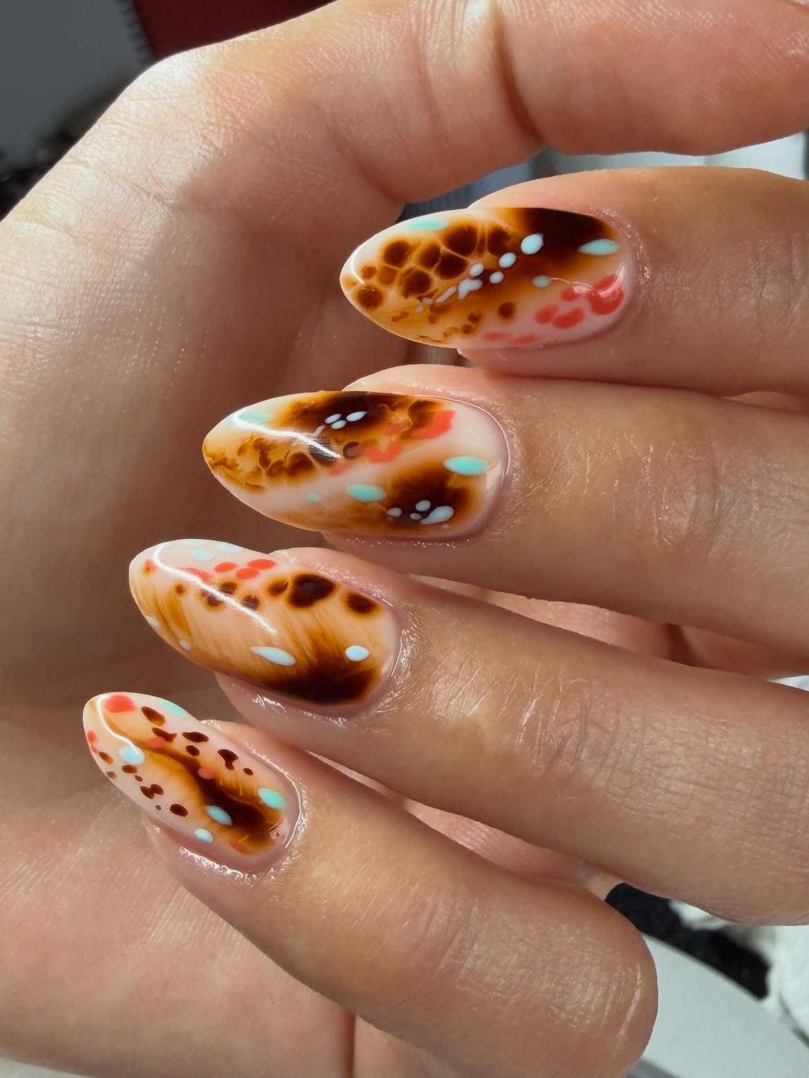 Glossy almond nails with swirled brown, turquoise, coral, and cream patterns resembling a colorful ocean habitat