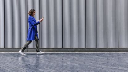 Female professional uses a smartphone while walking next to a building.